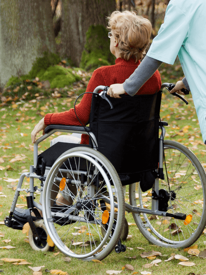 Pflegerin bei einem Spaziergang mit einer älteren Person im Rollstuhl