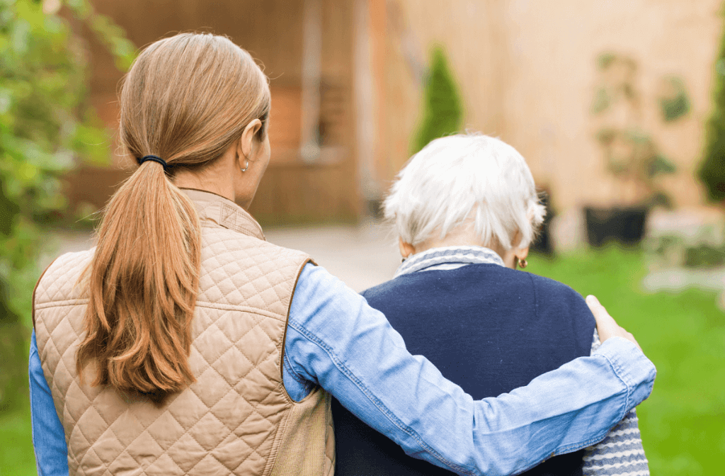 eine Pflegekraft umarmt eine ältere Person bei einem Spaziergang