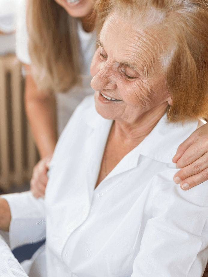 Pflegerin umarmt lächelnde ältere Person, die zu Hause sitzt