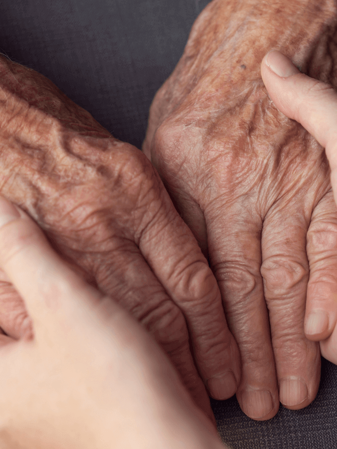 faltige Hände einer älteren Person, die von den Händen einer Pflegekraft gehalten werden
