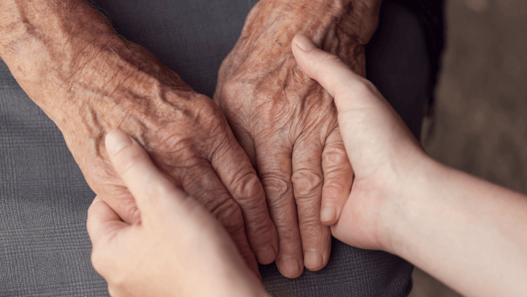 faltige Hände einer älteren Person, die von den Händen einer Pflegekraft gehalten werden